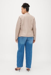 Μπεζ συνθετικό δερμάτινο μπουφάν με προσαρμοσμένη εφαρμογή, στρογγυλό γιακά και λεπτομέρειες στις ραφές, σε συνδυασμό με ανοιχτό μπλε φαρδιά τζιν παντελόνια και καφέ ψηλοτάκουνα παπούτσια.