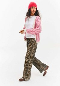 Červený proužkovaný kardigan s krémovými akcenty, bílé tričko a široké kalhoty s leopardím potiskem. Hnědé tenisky dokončují ležérní outfit.