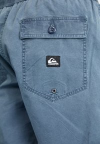 Blå kanvas shorts med en baklomme med knappelukking og en svart Quiksilver-logoapplikasjon. Strukturert stoff med et uformelt design.