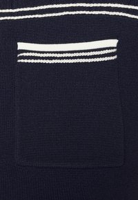 Granatowa tkanina o teksturze z prostokątną kieszenią z białymi paskami u góry i u dołu, podkreślającą warstwowy detal projektu.