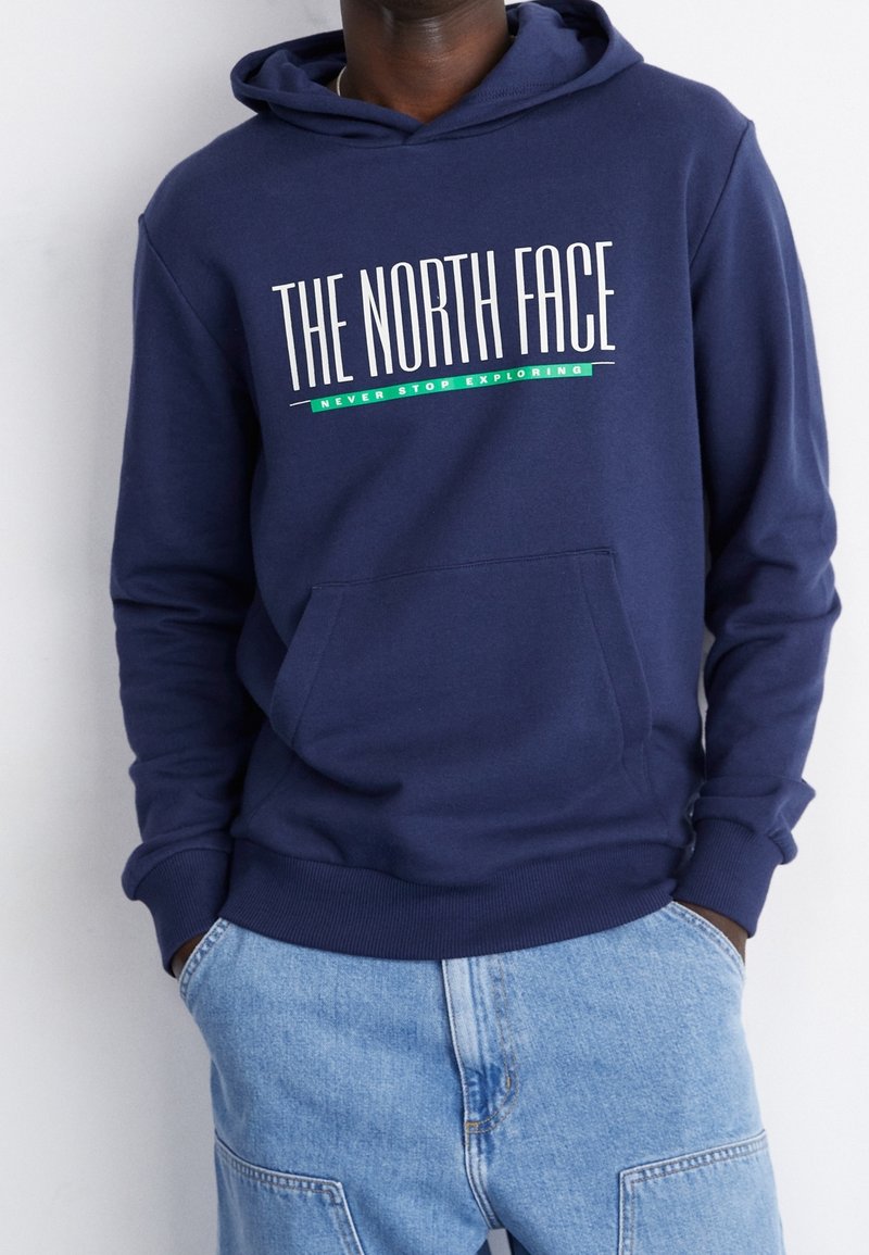 Mörkblå hoodie med framficka och ribbade muddar. Har "THE NORTH FACE"-logotyp i vitt och grönt. Bomullsblandat tyg, avslappnad passform.