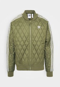 Olivgrüne gesteppte Jacke mit Reißverschluss vorne, gerippten Bündchen und zwei Seitentaschen. Mit weißen Streifen an den Ärmeln und dem Adidas-Logo versehen.