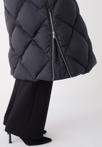 Schwarze Puffermantel mit gestepptem Diamantmuster und silbernen Reißverschlussdetails, kombiniert mit weit geschnittenen schwarzen Hosen und schwarzen High Heels.