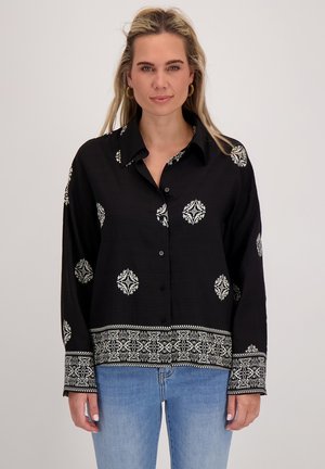 Zwarte lange mouw shirt met witte bloemenborduursels, knoopsluiting, kraag en gemusterde manchetten; lichte stof.