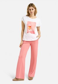 White short-sleeve t-shirt with a colorful graphic design featuring a drink. Paired with high-waisted, wide-leg pink pants. Brown sandals.