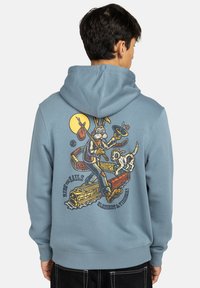 Felpa blu con grafica sul retro che raffigura un coniglio con una borsa e un cane, circondati da treni e da una luna gialla. Tessuto morbido in mistura di cotone, vestibilità ampia.
