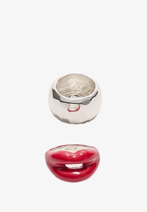 Two chunky rings on white background, one silver with a hammered texture, the other red shaped like glossy lips.