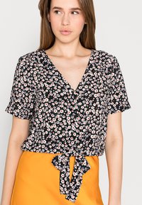 Blusa preta de mangas curtas com padrão floral; apresenta decote em V e um laço na cintura. O tecido é leve e texturizado.