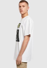 Hvid bomulds t-shirt med korte ærmer, der har et stort grafisk print i sort og gul på fronten, stylet med en løs pasform.