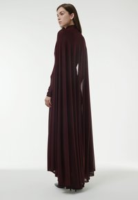 Bordeauxfarbenes, langärmeliges Kleid mit fließendem Cape-Design, ausgestattet mit strukturiertem Stoff und offenen Seitenpaneelen zur Belüftung.