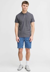 Pelēks īss piedurkņu polo krekls ar apkakli un trim pogām, kas savienots ar ceļa garuma ziliem denim šortiem. Modelis valkā pelēkus sporta apavus un baltas zeķes.