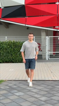 Avslappnad outfit med en ljusgrå randig kortärmad tröja, blå denimshorts och vita sneakers, som går på en belagd gångväg.