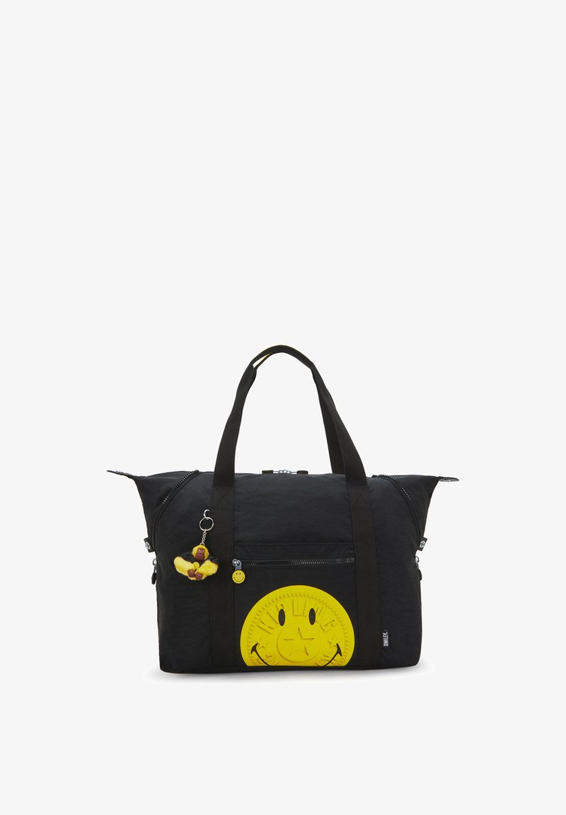 Sort duffeltaske med gul smileyansigtspatch og lille bamse-abe vedhæng hængende fra et håndtag.