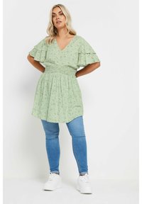 Light green dress with floral pattern, V-neckline, ruffled sleeves, and smocked waist. Paired with blue skinny jeans and white sneakers.