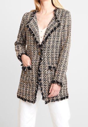 Blazer texturizado en negro, beige y crema; cuenta con borde de flecos, cuello con muescas y dos bolsillos delanteros. Botones cerca de la línea de la cintura.