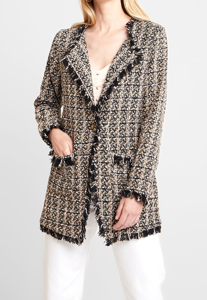 Texturerad kavaj i svart, beige och krämfärgad; har fransdetaljer, slagkrage och två framfickor. Knappar nära midjan.