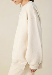 Pull beige clair à la coupe décontractée, doté de manches longues et volumineuses et d'un col rond. Texture douce et finitions côtelées.