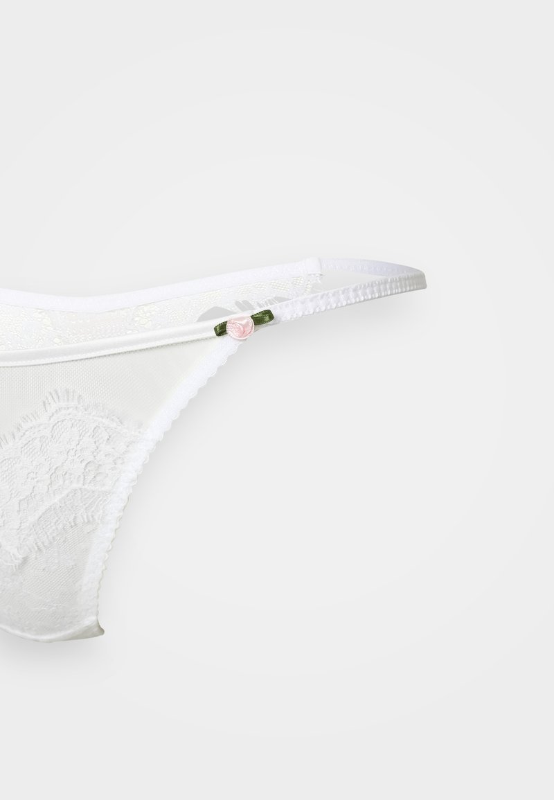 Vit spetsstring med ett blommönster, tunna elastiska remmar och en liten rosa ros som accent på en grön ögla. Transparent och delikat textur.