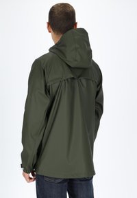 Olijfgroene waterdichte jas met capuchon, gladde textuur en versterkte schoudernaden, gezien vanaf de achterkant, gecombineerd met donkere spijkerbroek.