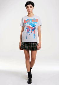 Gray cotton t-shirt featuring a retro graphic of Batman and Robin in blue and red. Worn with a black and green plaid skirt. Black shoes.
