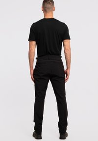 Schwarze Hosen mit schlanker Passform, aus leichtem Material gefertigt. Sie verfügen über eine glatte Textur, Gürtelschlaufen und Taschen auf der Rückseite.