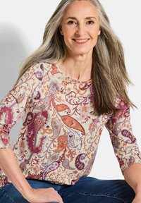 Langärmlige Bluse in Creme mit kompliziertem Paisley-Muster in Lila, Orange und Blau. Weicher Stoff mit rundem Ausschnitt und taillierter Passform.