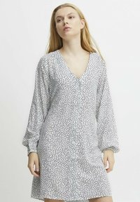 Weißes Kleid mit schwarz-gesprenkeltem Muster, V-Ausschnitt, langen Puffärmeln und Knopfleiste, aus leichtem Stoff gefertigt.