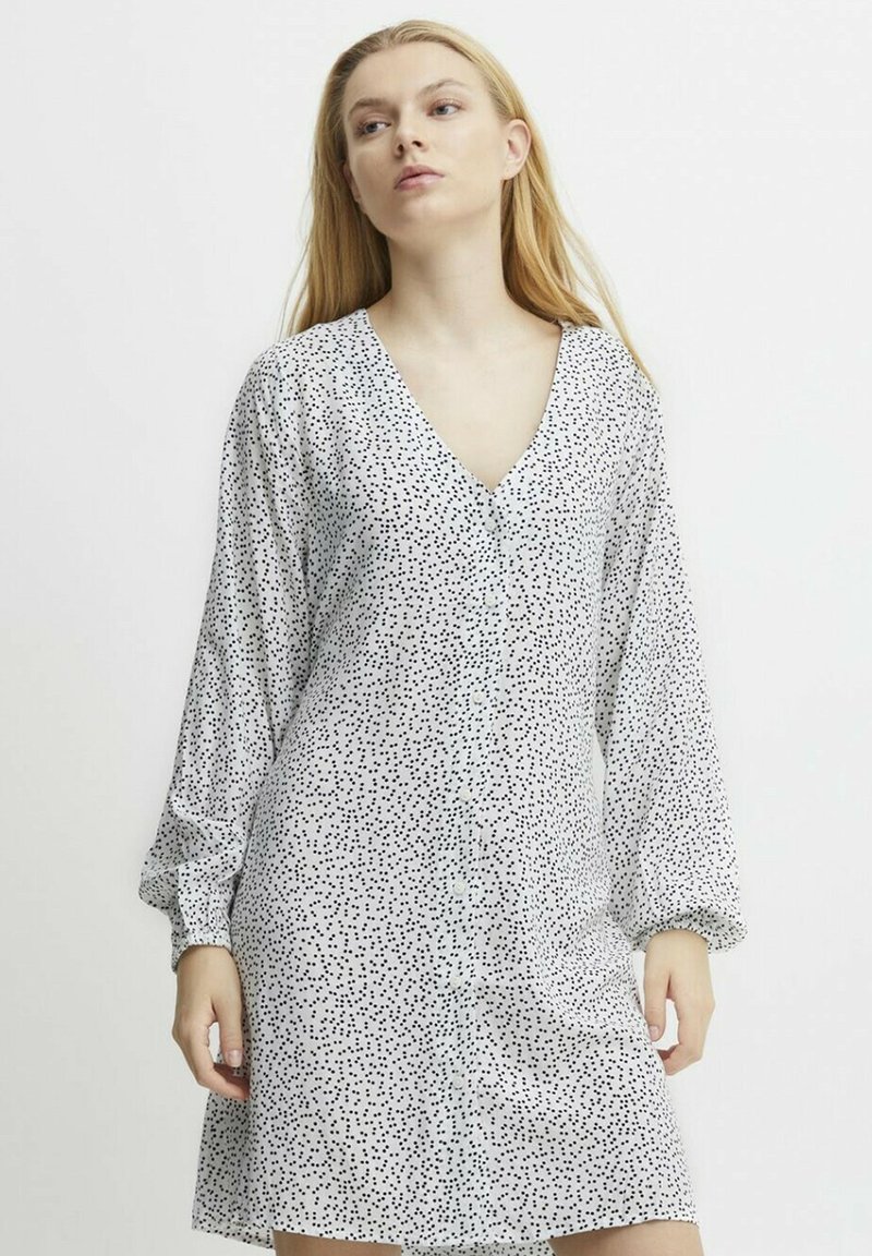 Weißes Kleid mit schwarz-gesprenkeltem Muster, V-Ausschnitt, langen Puffärmeln und Knopfleiste, aus leichtem Stoff gefertigt.