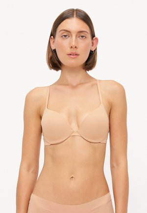 Beige bra with thin, adjustable straps, molded cups, and seamless design. Smooth fabric texture with a minimalistic and functional appearance.