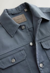 Veste en velours côtelé gris avec boutons-pression métalliques, poches poitrine à rabat et col replié, vue de face en haut.