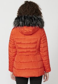 Oranžová puffová bunda s čiernou umelou kožušinou na kapucni, s horizontálne prešívanými panelmi a priliehavým strihom.