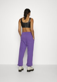 Černý kožený krátký top se zipem na zádech, doplněný fialovými tepláky s bočními kapsami a elastickými manžetami. Oblékaný s krémovými botami na platformě.