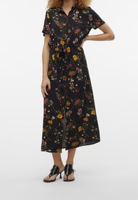 Blommig svart midiklänning med korta ärmar, knytning i midjan, livliga gula, röda och vita blommor på en mörk bakgrund, lättviktigt tyg.