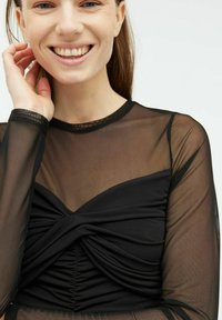 Sort mesh langærmet top med et snoet frontdesign, ruching-detaljer ved brystet og en tætsiddende silhuet.