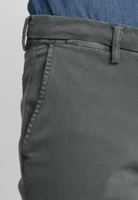 Šedé bavlněné kalhoty s rovnými nohavicemi, které mají hladkou texturu, boční kapsy a standardní pas.