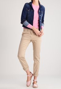 Jeansjacka med knappstängning, rosa tröja, beige chinos med uppvikta ben och rosa espadrilloskor med ankelremmar. Släta strukturer och avslappnad design.