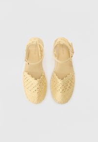 Espadrilles tissées jaunes avec un motif en croisillon, bout ouvert, et une sangle ajustable à la cheville avec une boucle métallique.