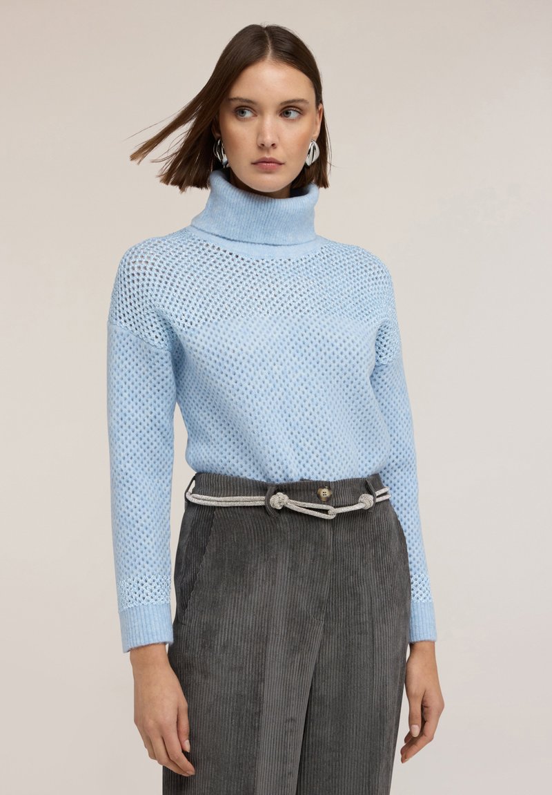 Ljusblå stickad tröja med hög krage, med ett nätmönster, ihop med mörkgrå kordverksbyxor med ett dekorativt bälte.