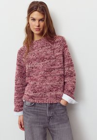 Pulover tricotat în nuanțe variate de roz, cu un model texturat. Are un decolteu rotund și manșete albe contrastante. Purtați cu blugi gri.