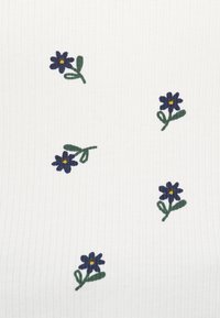 Λευκό ύφασμα με κατακόρυφη υφή που έχει διάσπαρτα σκούρα μπλε κεντήματα λουλουδιών, το καθένα με κίτρινο κέντρο και πράσινα φύλλα.