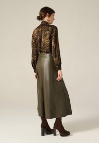 Blusa marrone a fantasia con collo alto, abbinata a una gonna in pelle verde. La modella indossa sandali con tacco chunky e calzini marroni a coste.
