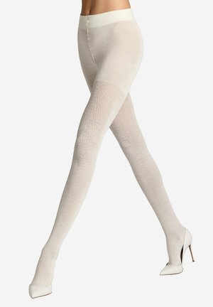 Beine mit cremefarbenen gemusterten Strumpfhosen und weißen High Heels, wobei ein Bein vor dem anderen gekreuzt ist.