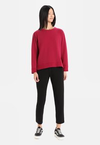 Sudadera roja de manga larga y corte holgado, combinada con pantalones negros ajustados y zapatillas negras con detalles en blanco.