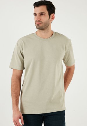 Tricou scurt cu mânecă în culoarea verde măsline deschis, dintr-un material moale din bumbac, cu un guler rotund și o croială lejeră, asortat cu blugi închis.