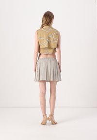 Arany- és fehér színű geometrikus mintás len crop top, bézs és fehér pöttyös, pliszírozott szoknyával párosítva. Átlátszó sarkú cipő látható.