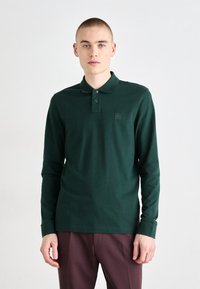 Polo cu mânecă lungă din bumbac verde închis, cu guler clasic, placket cu două butoane și o mică etichetă cu logo pe piept.