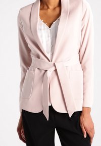 Ljusrosa kavaj med sjalkrage, bältesmidjad midja och två framfickor. Slät tyg med skräddarsydd passform och enhetlig färg.