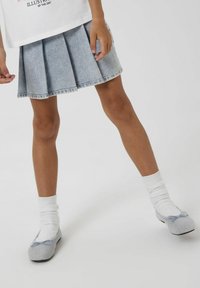 Svetlo modra denim krilo z naborki, ki sega nad kolenom, v kombinaciji s sivimi slip-on čevlji in belimi gležnjarji. Enostaven dizajn in mehak material.