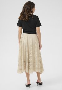 Gonna midi beige in pizzo con intricati motivi floreali, texture trasparente e vita alta, abbinata a una maglietta nera a maniche corte.