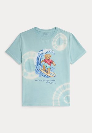 T-shirt tie-dye bleu clair avec un ours surfant sur une vague, portant une chemise rouge et un short aqua, avec le texte « Polo Bear by Ralph Lauren » en dessous.